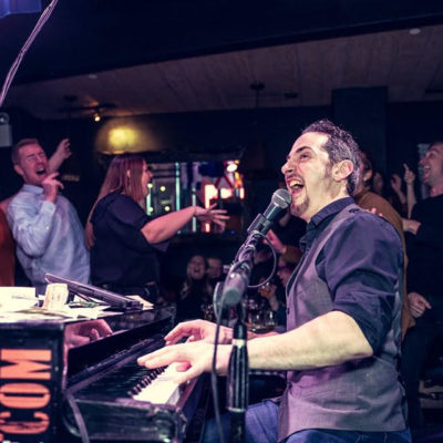 Piano man Mark Weiser singing and playing to a the crowd at a dueling pianos show.