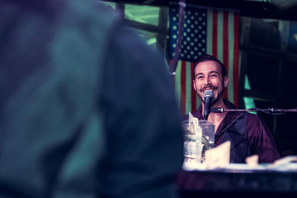 Piano man smiles with flag in the background