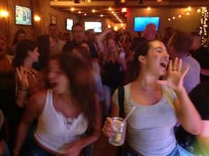 Two girls at a bachelorette's party dance in the foreground of the crowd at a dueling pianos show.