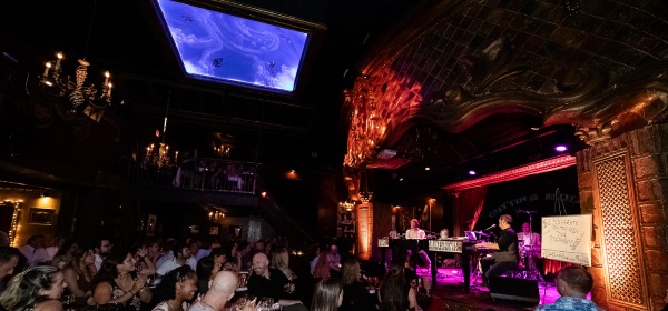 2 Dueling pianists play on a multicolored stage to a packed crowd at a Saturday night show in NYC.