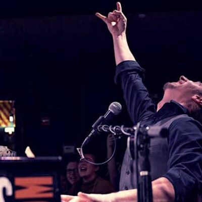 The piano player points his fingers to the sky at a Dueling Pianos show.